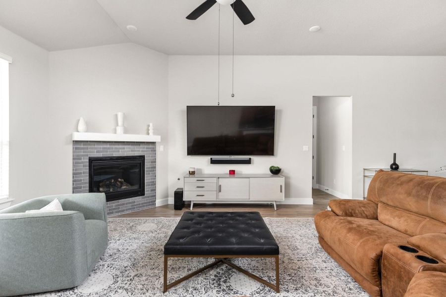 Living room featuring a brick fireplace, light wood-style flooring, ceiling fan, and lofted ceiling