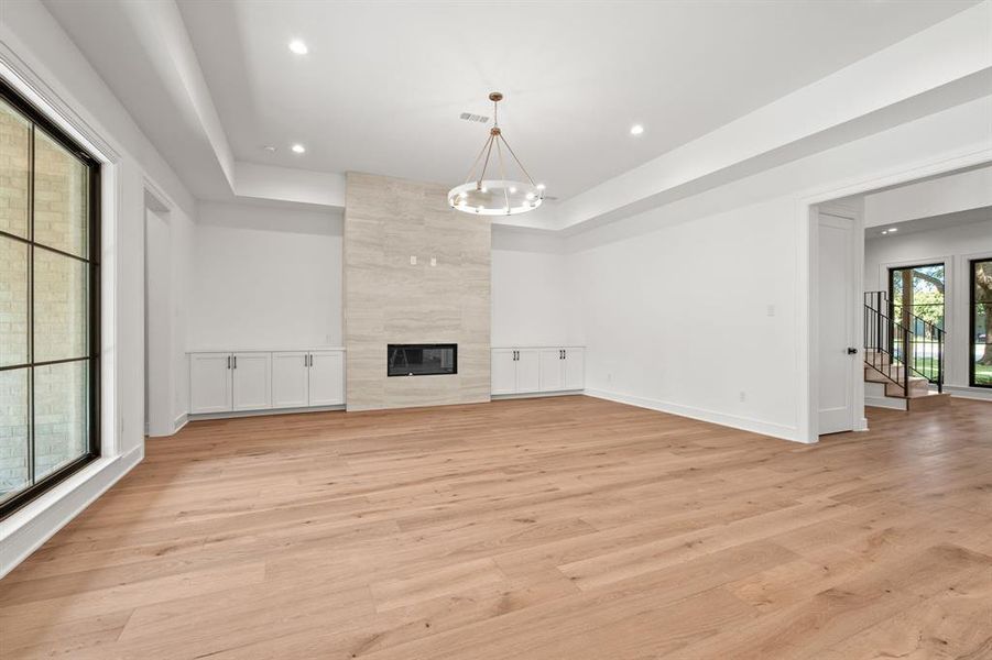 Unfurnished living room featuring light wood-type flooring, recessed lighting, a chandelier, a premium fireplace, and a raised ceiling Unfurnished living room featuring light wood-type flooring, recessed lighting, a chandelier, a premium fireplace, and a raised ceiling