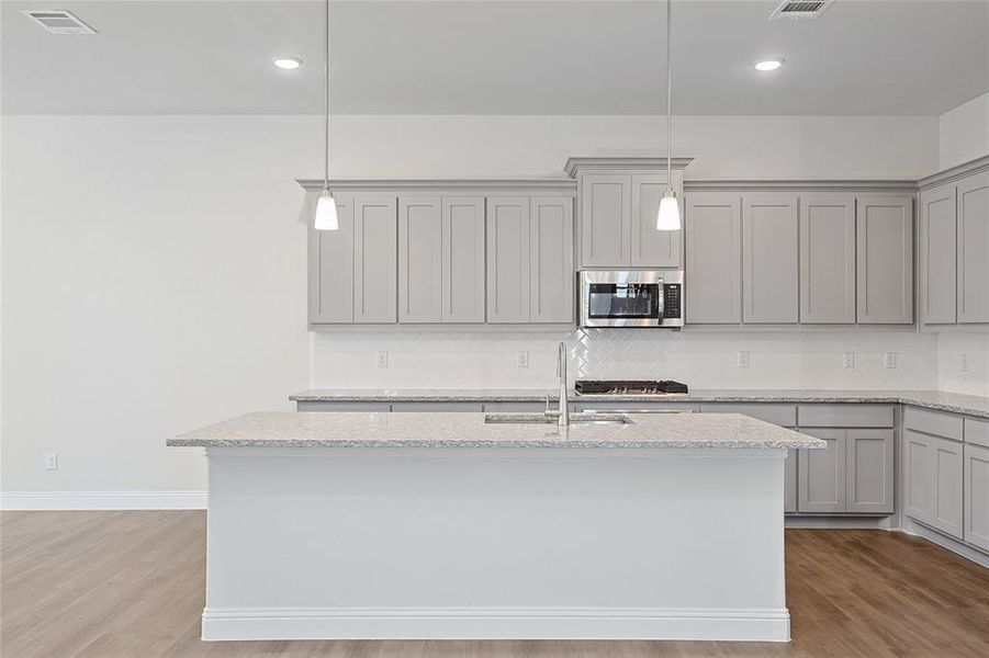 Kitchen with gray cabinetry, pendant lighting, light stone counters, light wood-style flooring, and stainless steel appliances Kitchen with gray cabinetry, pendant lighting, light stone counters, light wood-style flooring, and stainless steel appliances
