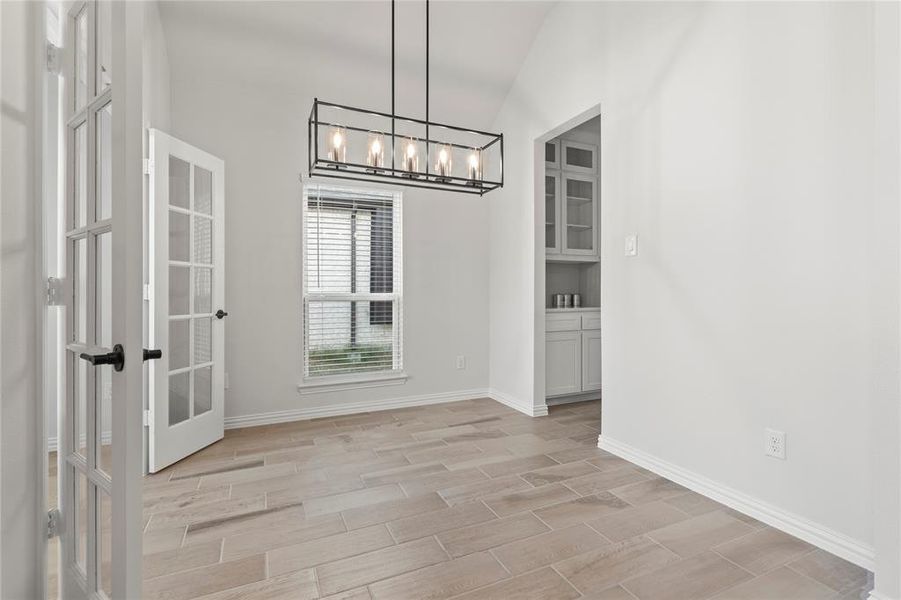 Unfurnished dining area featuring a notable chandelier, french doors, and vaulted ceiling