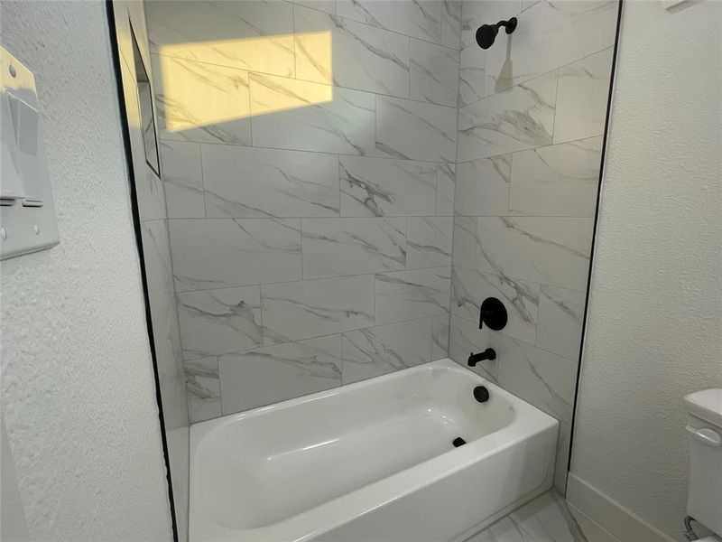 Full bathroom featuring a textured wall and shower / tub combination