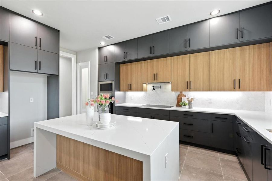 Kitchen featuring stainless steel microwave, decorative backsplash, light tile patterned flooring, a kitchen island, and light stone countertops