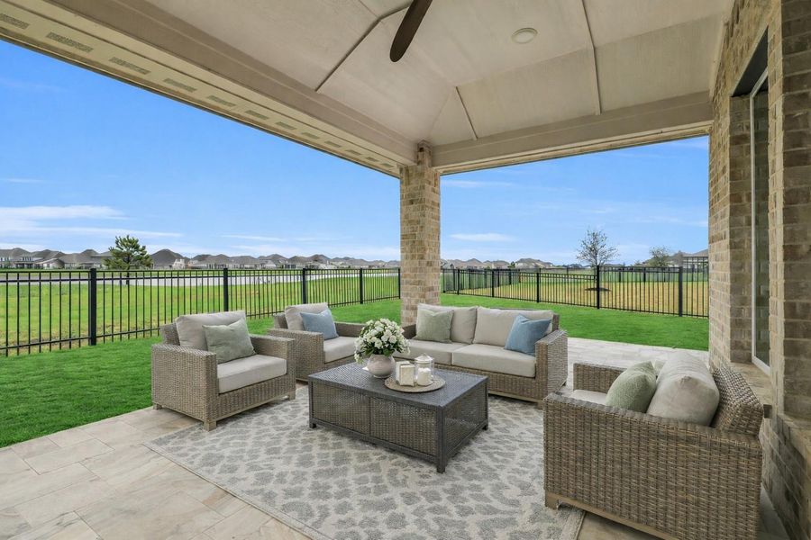 Virtually staged covered patio designed for outdoor living, featuring a comfortable seating area with tranquil lake views—perfect for relaxing or entertaining while enjoying the expansive backyard and peaceful waterfront setting.