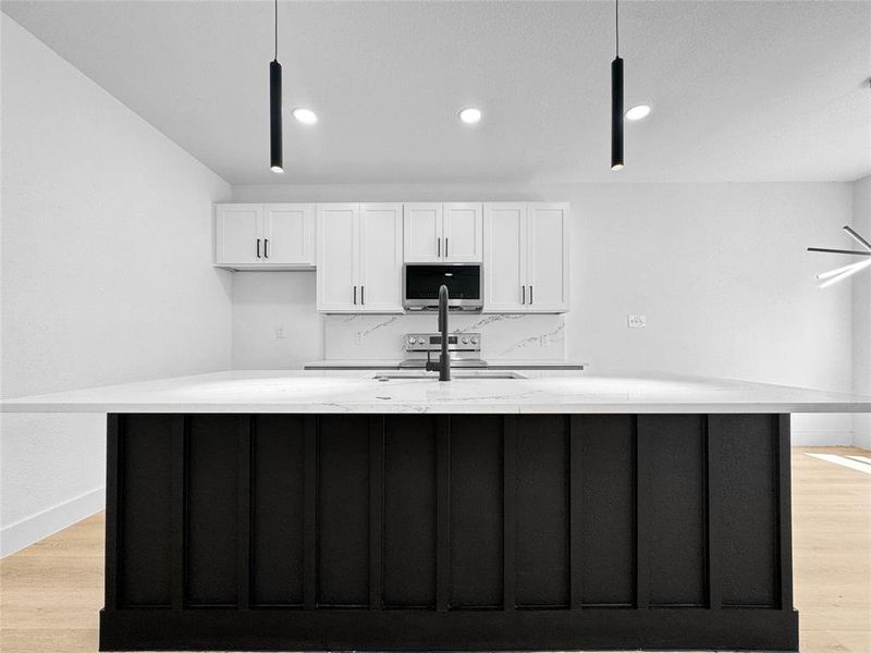 Kitchen featuring light wood-style floors, white cabinetry, an island with sink, light stone countertops, and recessed lighting