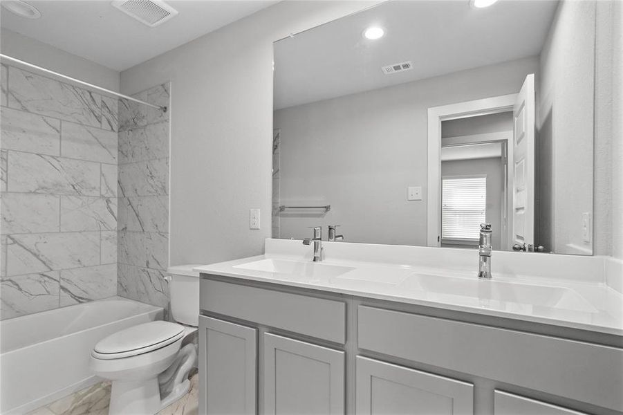 Secondary bath features tile flooring, bath/shower combo with tile surround, stained cabinets, beautiful light countertops, mirror, sleek fixtures and modern finishes.