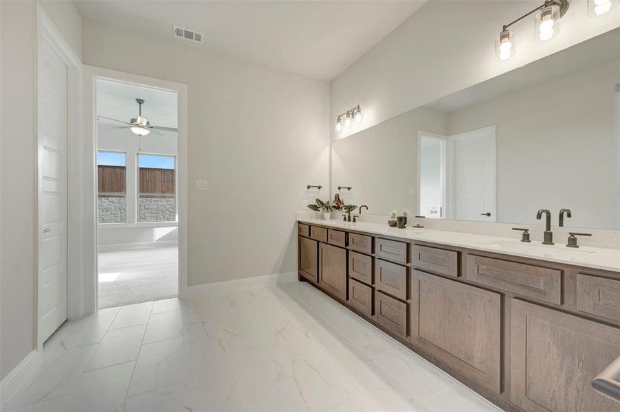 Dual vanity with wood-finish cabinetry, light-toned countertops, and matte black fixtures