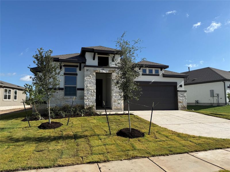Prairie-style home with stone siding, stucco siding, concrete driveway, and a front yard Prairie-style home with stone siding, stucco siding, concrete driveway, and a front yard