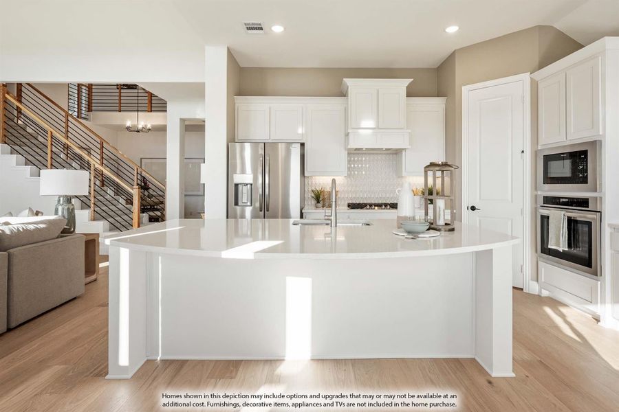 Open kitchen with curved white island, white cabinets, stainless appliances, and light wood floors Open kitchen with curved white island, white cabinets, stainless appliances, and light wood floors