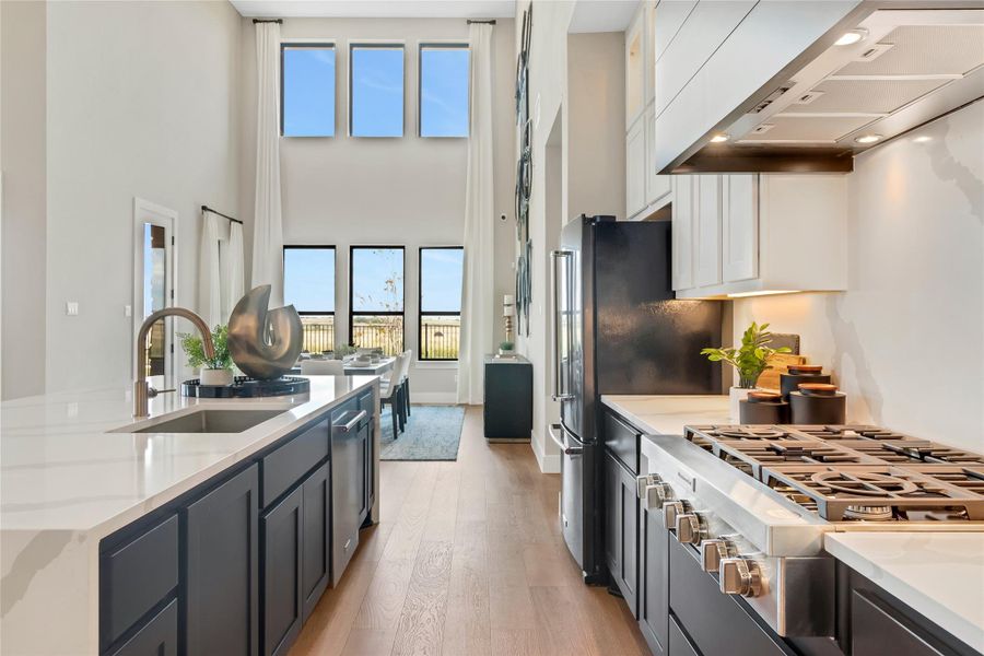 Kitchen featuring range hood, stainless steel appliances, light wood-style flooring, white cabinetry, and a kitchen island with sink Kitchen featuring range hood, stainless steel appliances, light wood-style flooring, white cabinetry, and a kitchen island with sink