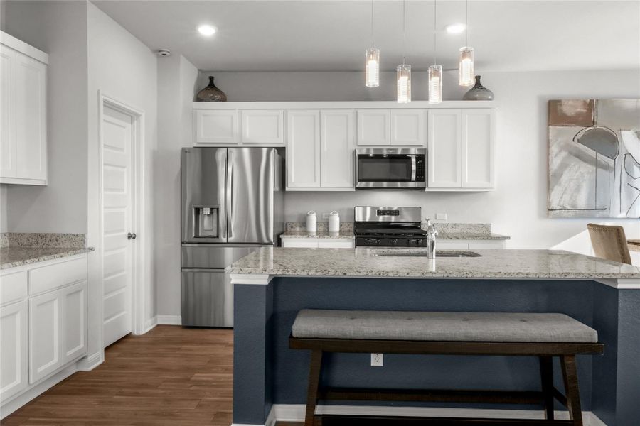 Kitchen featuring white cabinets, stainless steel appliances, light stone countertops, decorative light fixtures, and recessed lighting