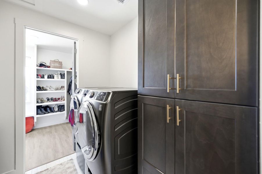 Functional design highlights this modern laundry space featuring built-in cabinetry and direct closet access.