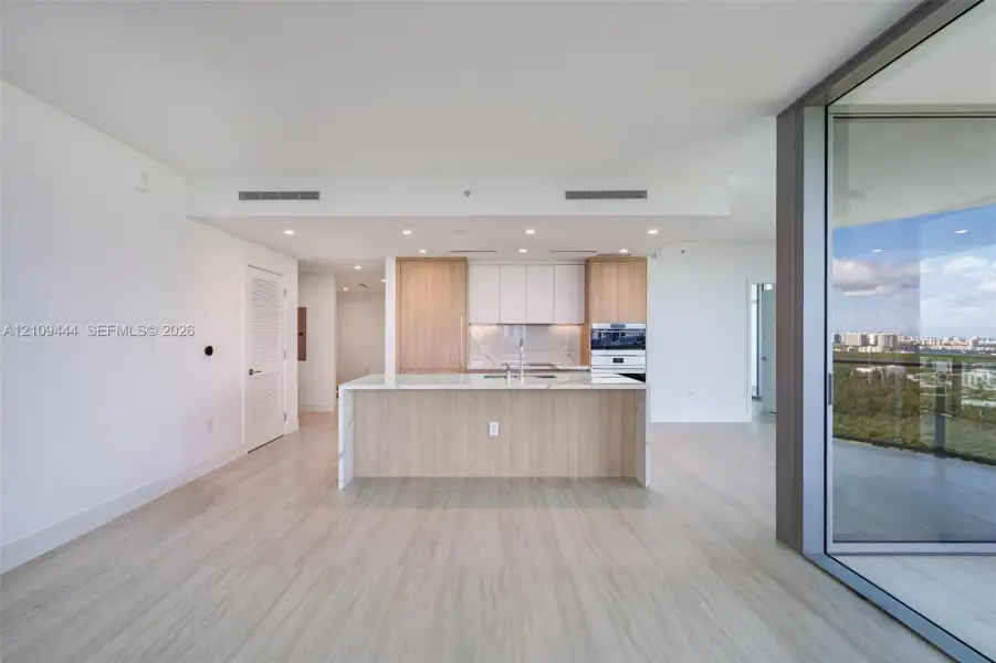 Kitchen featuring an island with stone-finish countertop, wood-finish cabinetry, built-in stainless steel wall oven, recessed lighting, and expansive floor-to-ceiling glass sliding doors