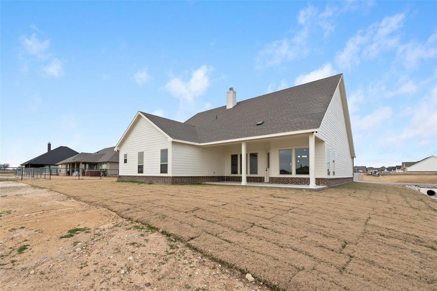 Rear view of property featuring a patio, a chimney, a shingled roof, and brick siding