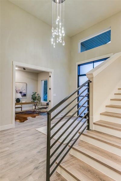 Staircase featuring LVP light wood floors, a chandelier, and a towering ceiling Staircase featuring LVP light wood floors, a chandelier, and a towering ceiling