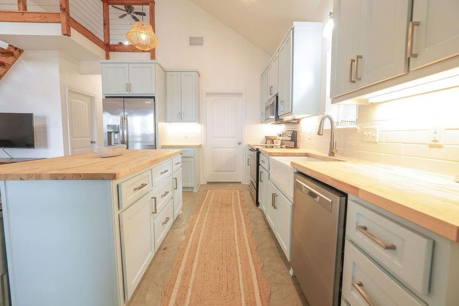 Kitchen with butcher block counters, stainless steel appliances, a center island, decorative light fixtures, and backsplash
