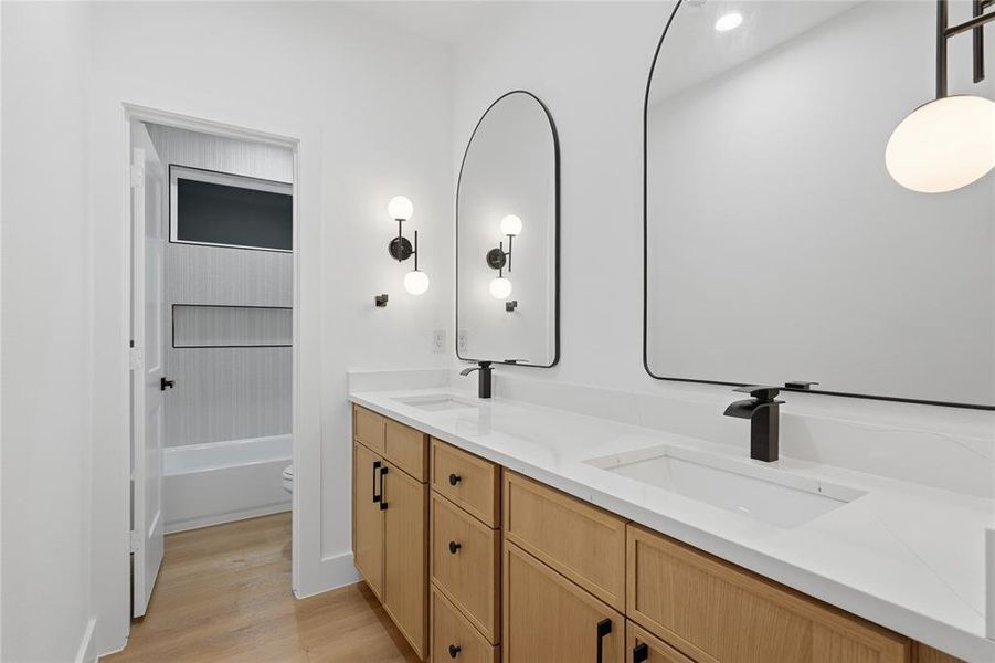 Dual vanity with light wood-finish cabinetry, white countertops, and integrated rectangular sinks Dual vanity with light wood-finish cabinetry, white countertops, and integrated rectangular sinks