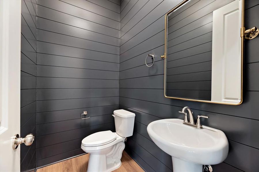 Bathroom with toilet, hardwood / wood-style flooring, wood walls, and sink