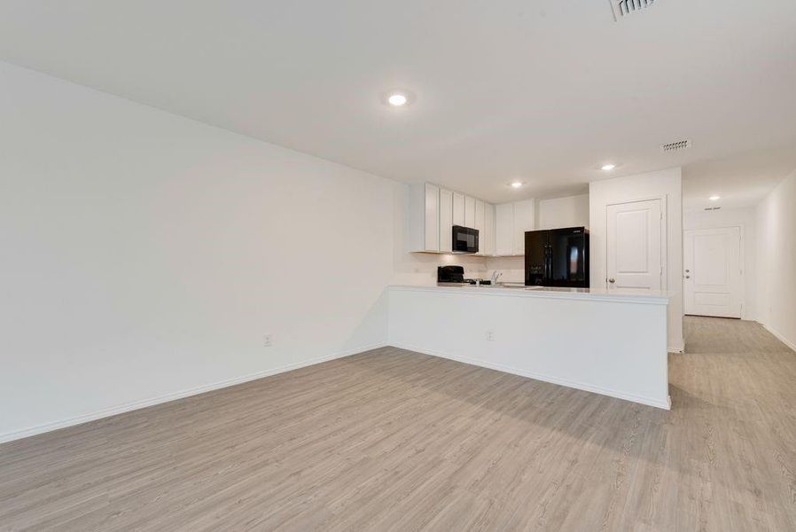 Kitchen with baseboards, visible vents, light wood-type flooring, black appliances, and white cabinetry