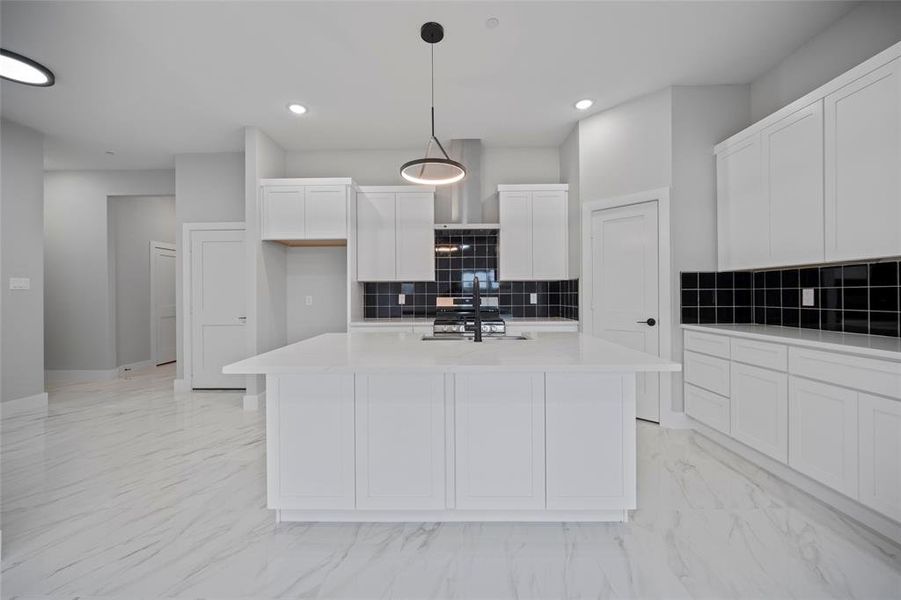 Kitchen featuring marble finish floor, an island with sink, decorative light fixtures, white cabinetry, and light countertops