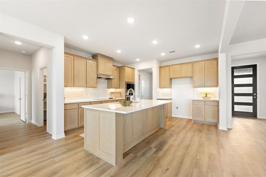 Kitchen with light brown cabinetry, a center island with sink, light wood-type flooring, recessed lighting, and under cabinet range hood