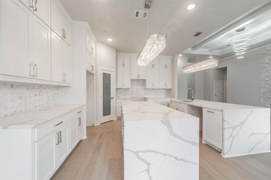 Kitchen featuring a kitchen island with sink, light stone counters, white cabinets, light wood-style floors, and recessed lighting