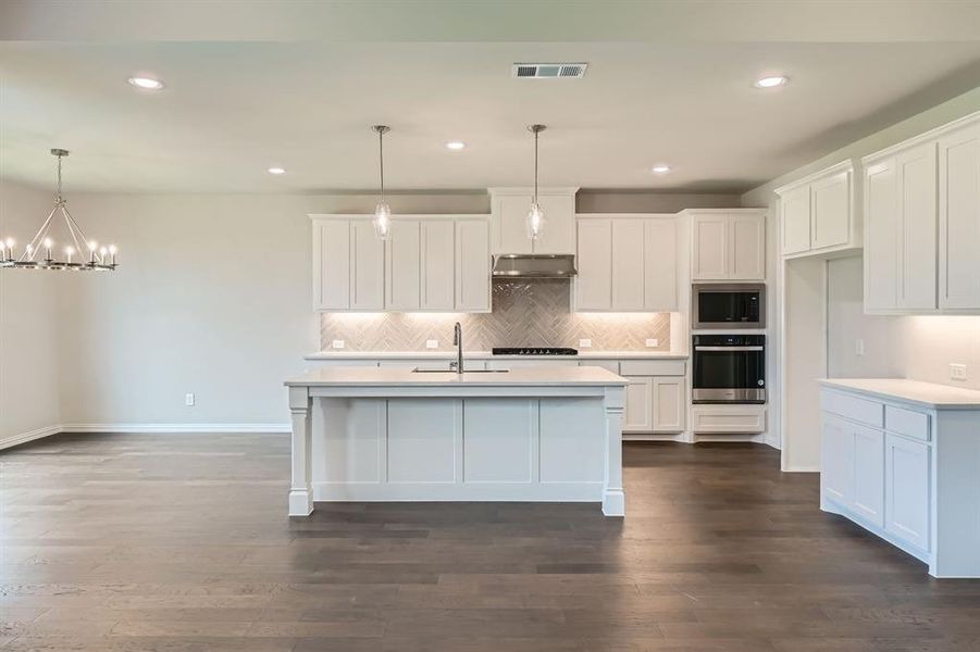 Kitchen featuring white cabinets, appliances with stainless steel finishes, hanging light fixtures, and a center island with sink