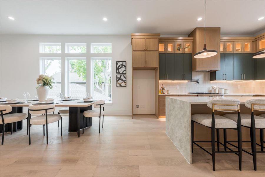 Green gets a serious seat at the table. Paired with oak, anchored by a waterfall stone island, and lit from within the glass uppers, this palette moves past trend into territory that will still look current in ten years. The color is the risk; the execution is the reassurance.