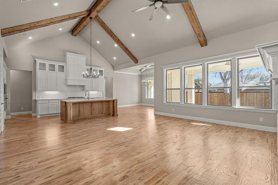 Unfurnished living room featuring plenty of natural light, high vaulted ceiling, ceiling fan with notable chandelier, and light wood-type flooring