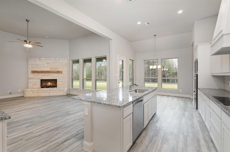 Kitchen with dishwasher, a center island with sink, white cabinets, and a fireplace