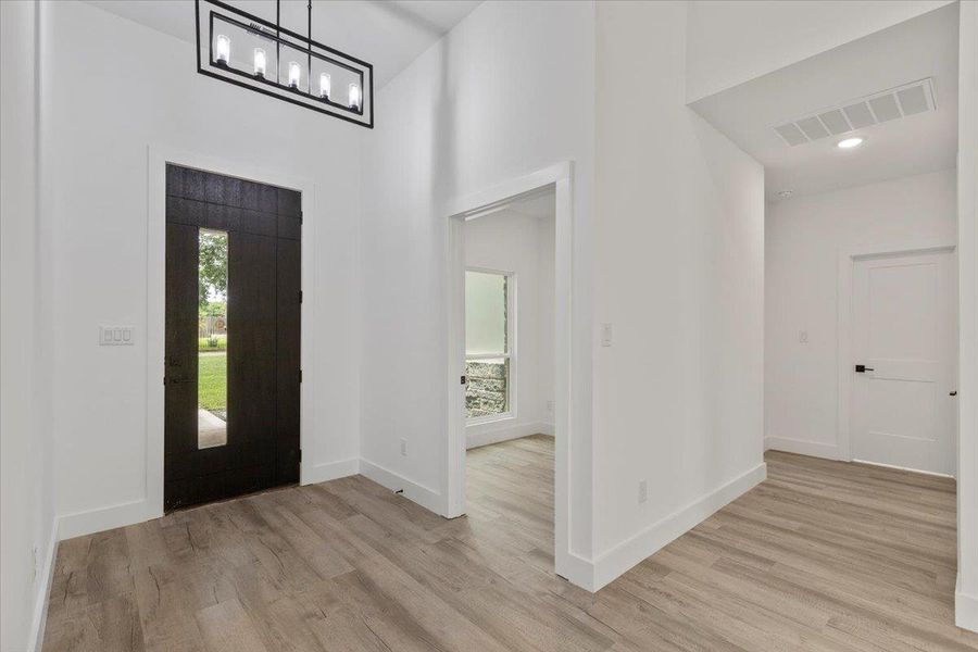 Foyer entrance featuring a high ceiling, light wood finished floors, and a chandelier Foyer entrance featuring a high ceiling, light wood finished floors, and a chandelier