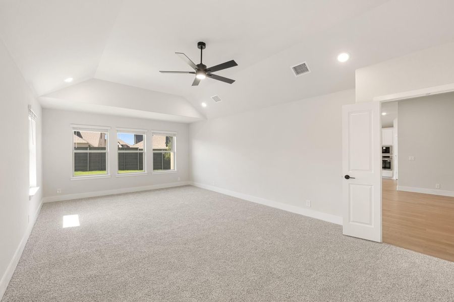 Empty bedroom with vaulted ceiling, black ceiling fan, carpet flooring, and triple window overlooking backyard