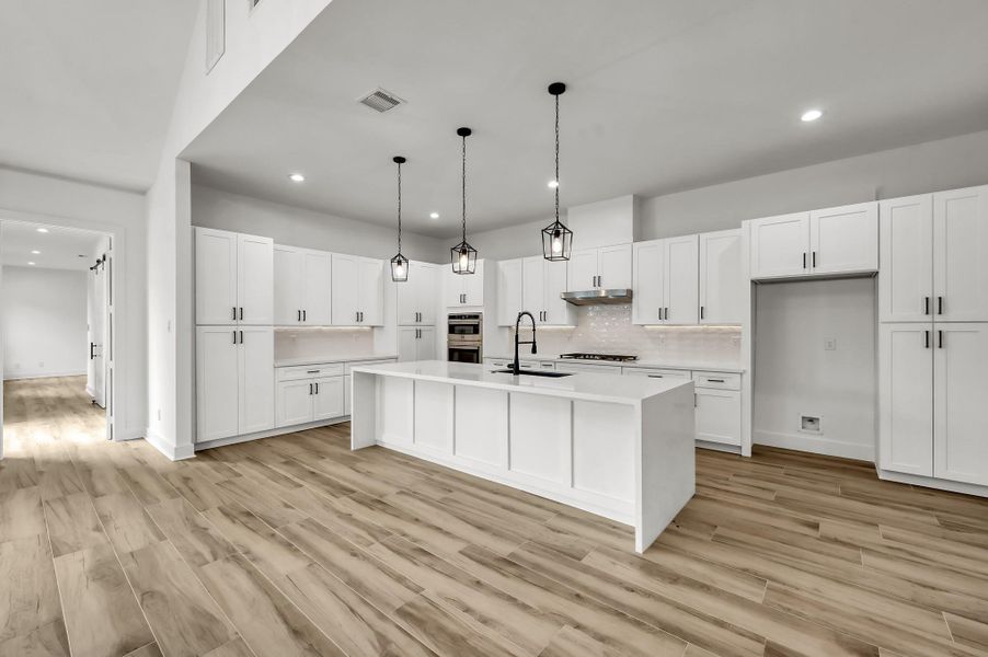 Bright and airy kitchen featuring extensive cabinetry, modern lighting, and a large center island ideal for gathering and meal preparation.
