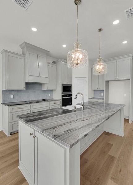 Kitchen featuring light wood-type flooring, light stone countertops, a large island with sink, decorative backsplash, and recessed lighting
