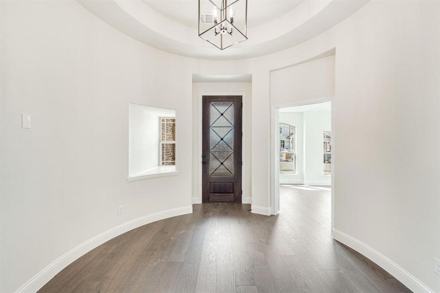 Entryway featuring dark wood-style flooring, a chandelier, and a raised ceiling