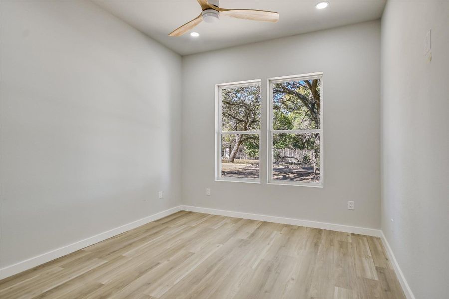A quiet bedroom retreat with tree-filled views, warm flooring, and a modern ceiling fan.