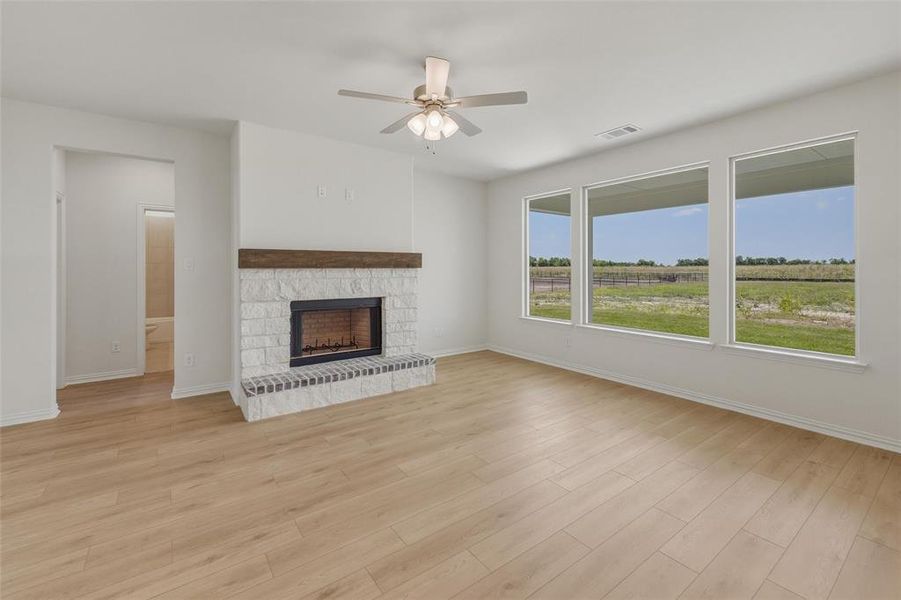 Living space featuring a whitewashed brick fireplace with a wood-finish mantel, light wood-finish flooring, and a ceiling fan with integrated lighting Living space featuring a whitewashed brick fireplace with a wood-finish mantel, light wood-finish flooring, and a ceiling fan with integrated lighting