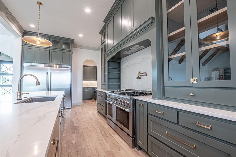 Kitchen with glass insert cabinets, crown molding, pendant lighting, high end appliances, and light stone countertops Kitchen with glass insert cabinets, crown molding, pendant lighting, high end appliances, and light stone countertops