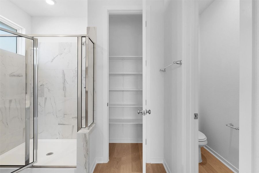 Bathroom with a marble finish shower, light wood-style flooring, and a walk in closet Bathroom with a marble finish shower, light wood-style flooring, and a walk in closet