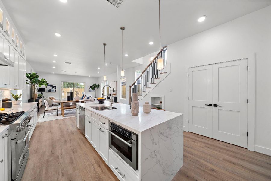 This modern open-concept space features a sleek kitchen with a large island, 10 ft. long quartz island, and stainless steel appliances. It flows into a bright living area with natural light and a view of the staircase, creating an inviting atmosphere. This modern open-concept space features a sleek kitchen with a large island, 10 ft. long quartz island, and stainless steel appliances. It flows into a bright living area with natural light and a view of the staircase, creating an inviting atmosphere.