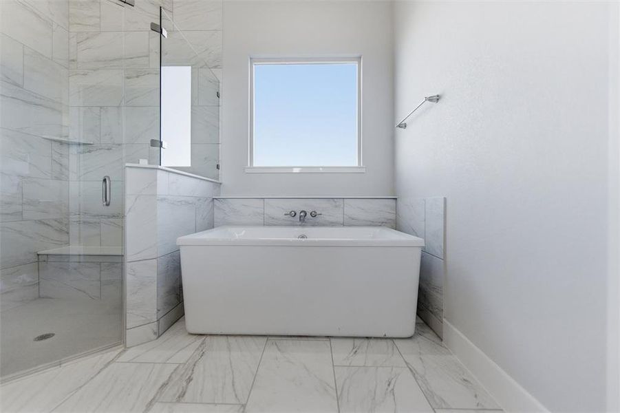 Bathroom with a marble finish shower, a soaking tub, light marble finish floors, and tile walls