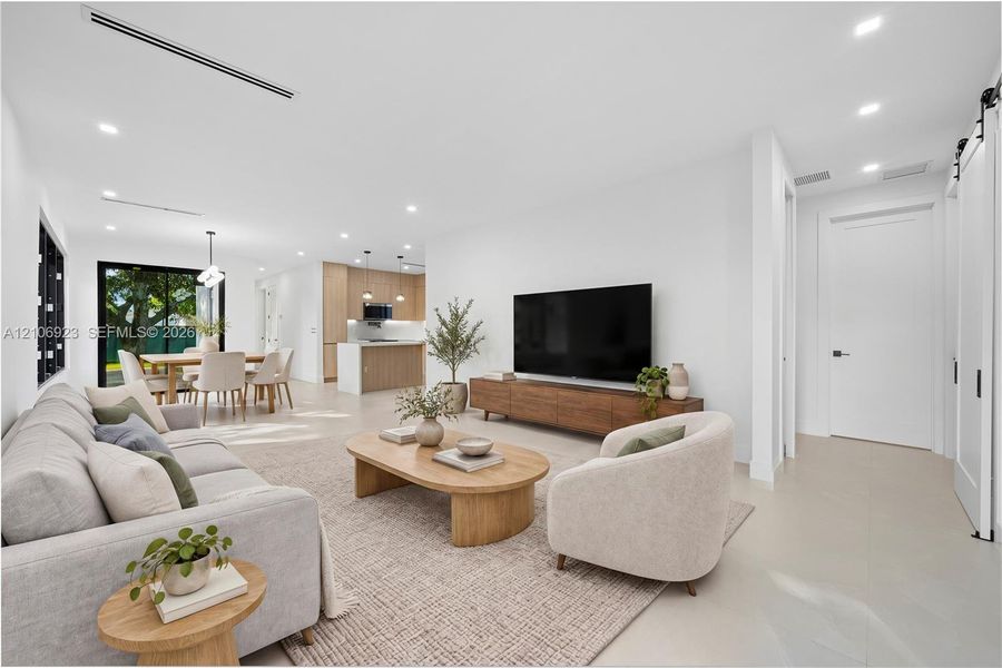 Open-concept interior featuring light-toned flooring, recessed lighting, linear HVAC diffusers, white sliding barn door, and kitchen cabinetry with wood-finish accents Open-concept interior featuring light-toned flooring, recessed lighting, linear HVAC diffusers, white sliding barn door, and kitchen cabinetry with wood-finish accents