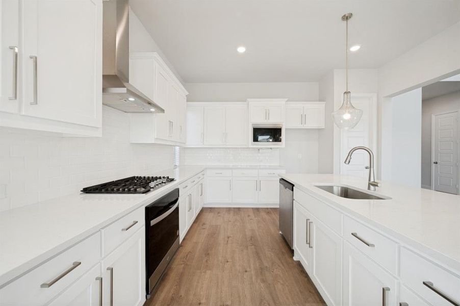 Contemporary kitchen featuring white cabinetry, light-toned countertops, wood-finish flooring, stainless steel appliances, and a central island with an undermount sink
