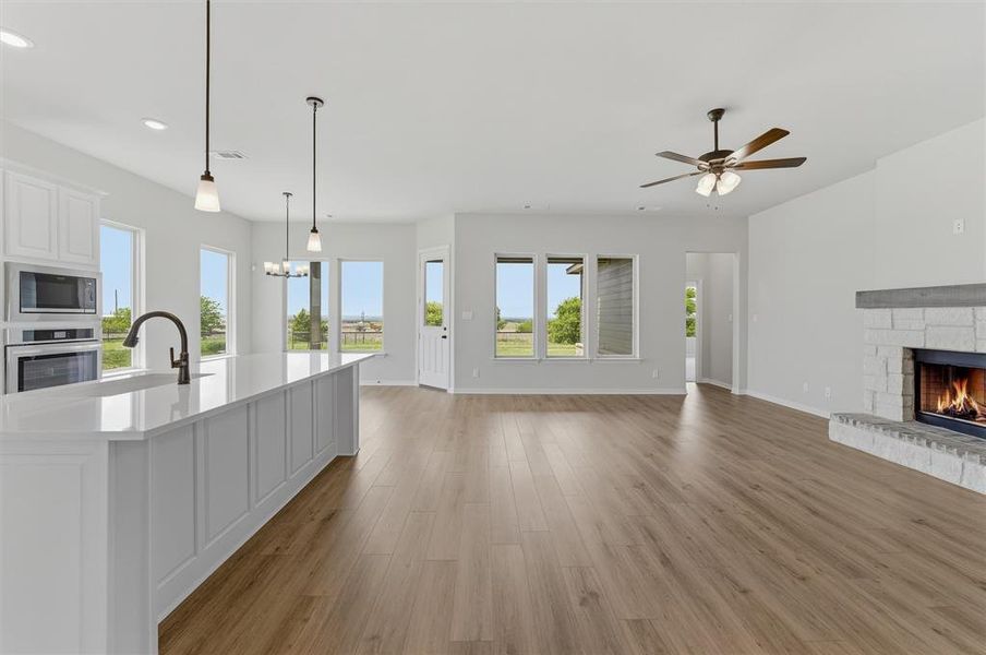 Unfurnished living room with a stone fireplace, dark wood finished floors, a chandelier, and a ceiling fan Unfurnished living room with a stone fireplace, dark wood finished floors, a chandelier, and a ceiling fan