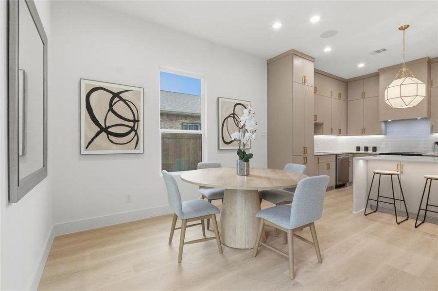 Open-concept kitchen and dining area featuring light wood-finish flooring, recessed lighting, and a window providing natural illumination Open-concept kitchen and dining area featuring light wood-finish flooring, recessed lighting, and a window providing natural illumination