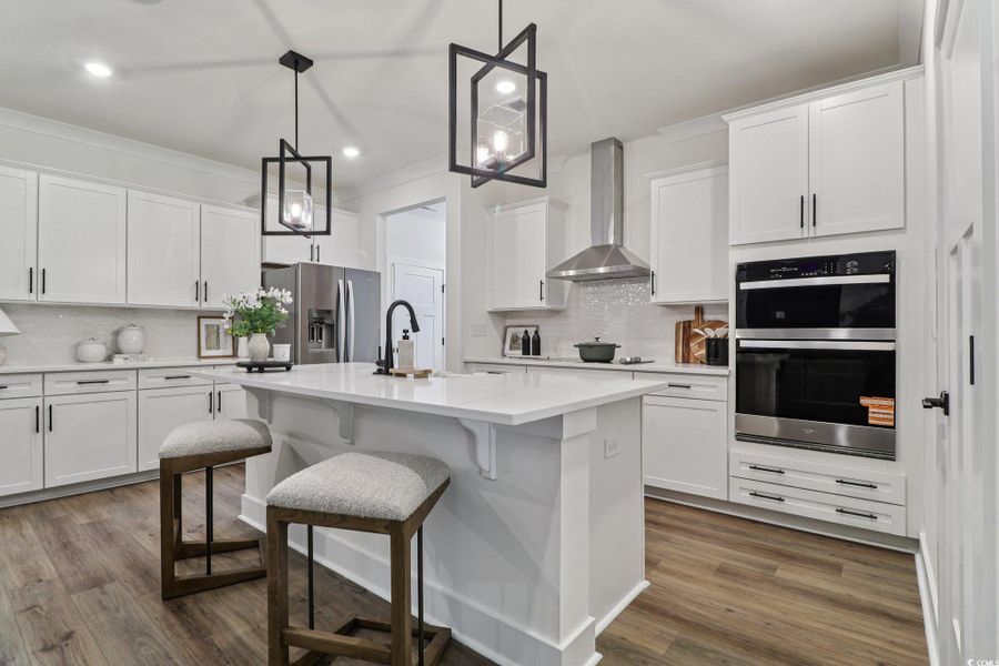 Kitchen featuring tasteful backsplash, white cabinetry, wall chimney range hood, a kitchen bar, and recessed lighting