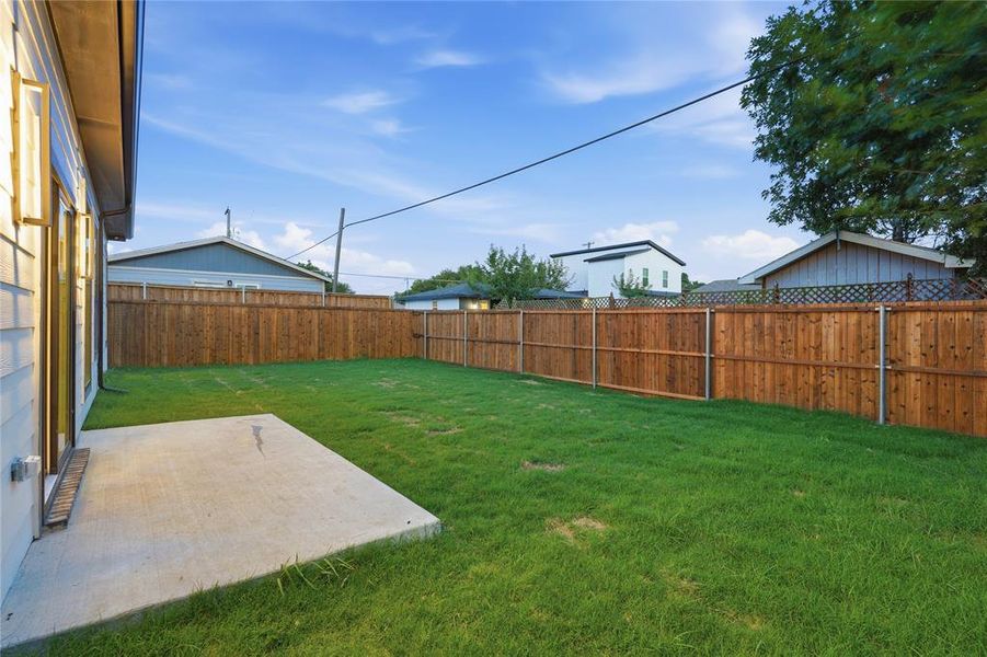 Expansive green lawn featuring a privacy fence, concrete patio, and exterior siding