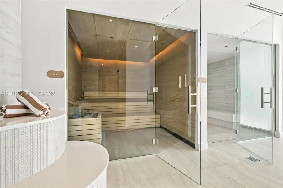 Custom sauna featuring wood-panelled interior, multi-level bench seating, and glass enclosure, paired with a glass-enclosed steam shower featuring neutral-toned wall tiles and tile flooring Custom sauna featuring wood-panelled interior, multi-level bench seating, and glass enclosure, paired with a glass-enclosed steam shower featuring neutral-toned wall tiles and tile flooring
