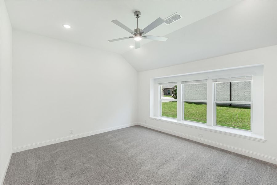 Empty bedroom with gray carpet, vaulted ceiling, ceiling fan, and large triple window overlooking yard Empty bedroom with gray carpet, vaulted ceiling, ceiling fan, and large triple window overlooking yard