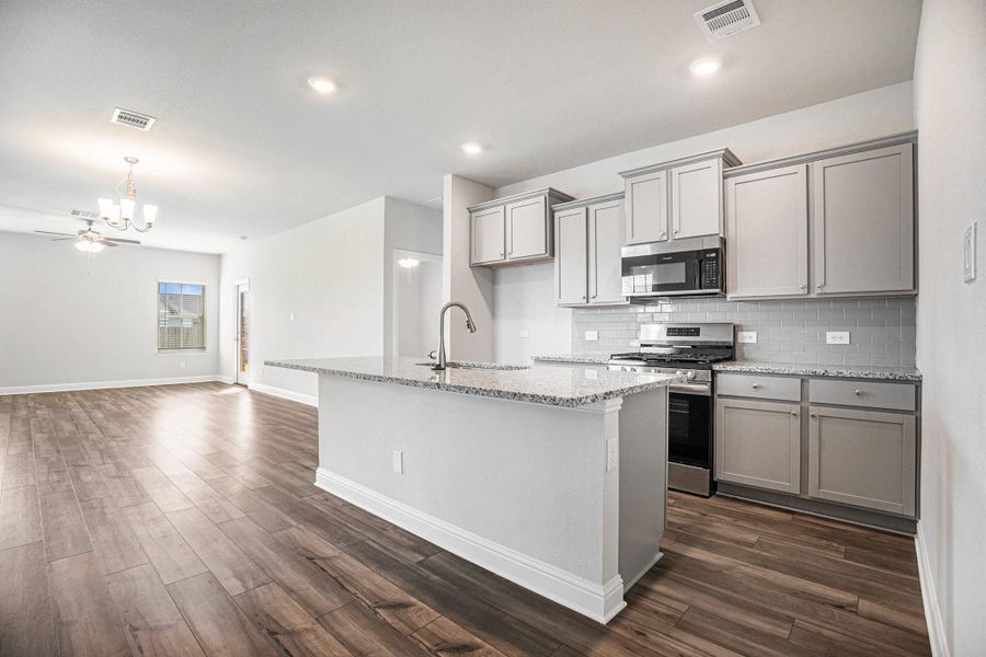 This photo showcases a modern open-concept kitchen and living area. The kitchen features granite countertops, stainless steel appliances, and light gray cabinetry. The space has luxury vinyl plank flooring, recessed lighting, and a ceiling fan, creating a bright and inviting atmosphere.