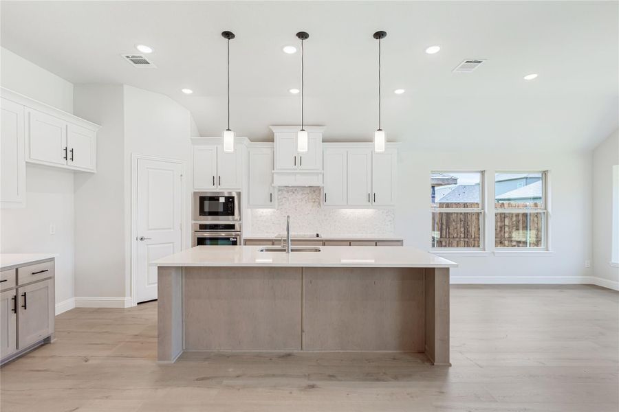Kitchen with large center island, white cabinets, pendant lights, and stainless steel appliances on light wood floors